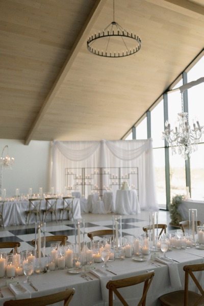A reception room at dusk, pillar candles running the length of the tables beneath iron and crystal chandeliers.